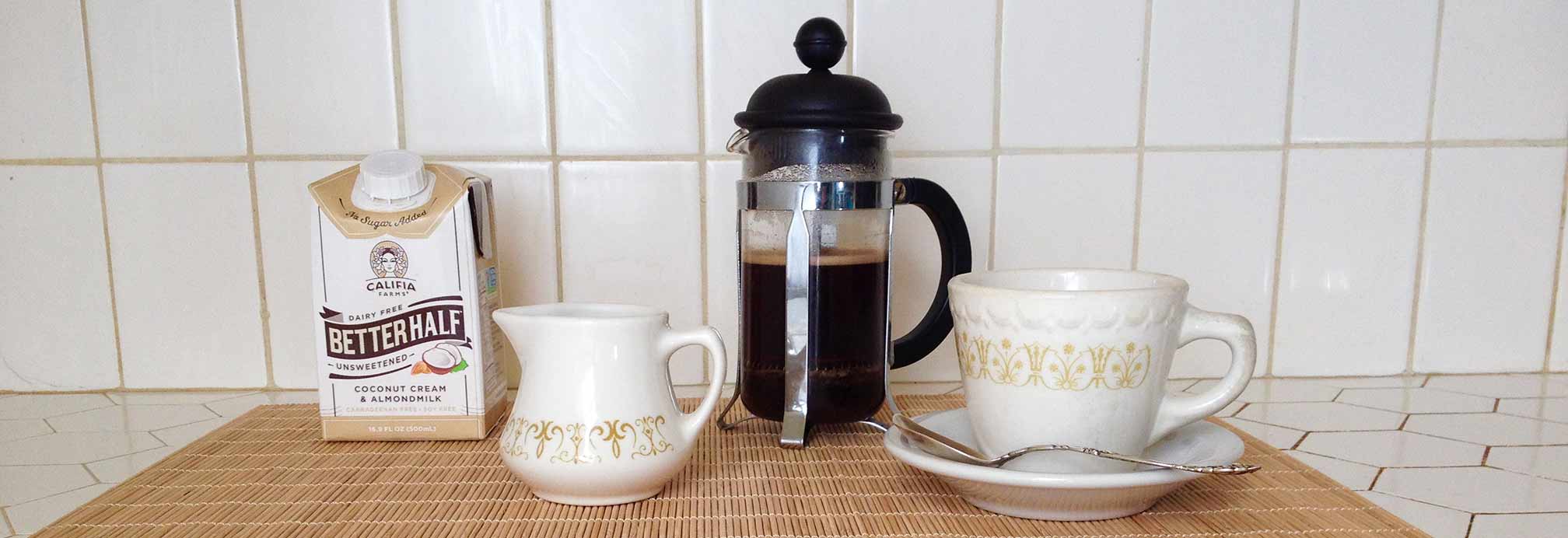 Better Half Coconut Cream & Almond Milk Unsweetened carton on tray with coffee maker, cup and milk pitcher.