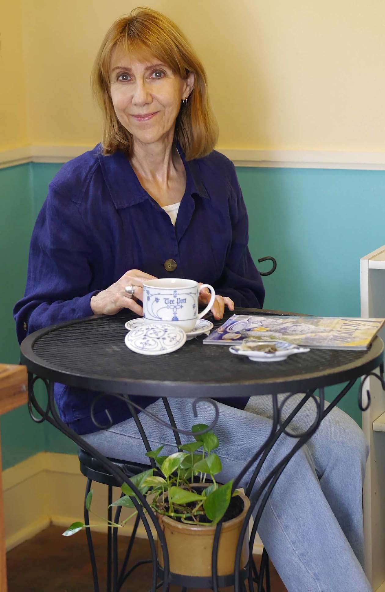Anne seated at bistro table with tea mug and magazine.