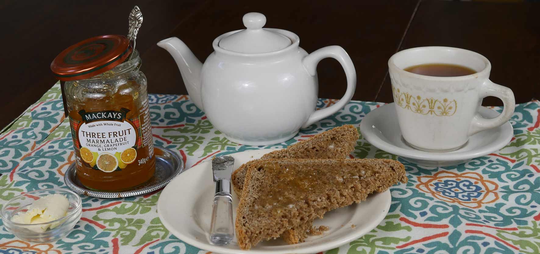 toast spread with marmalade, tea pot, tea cup, butter and spreader