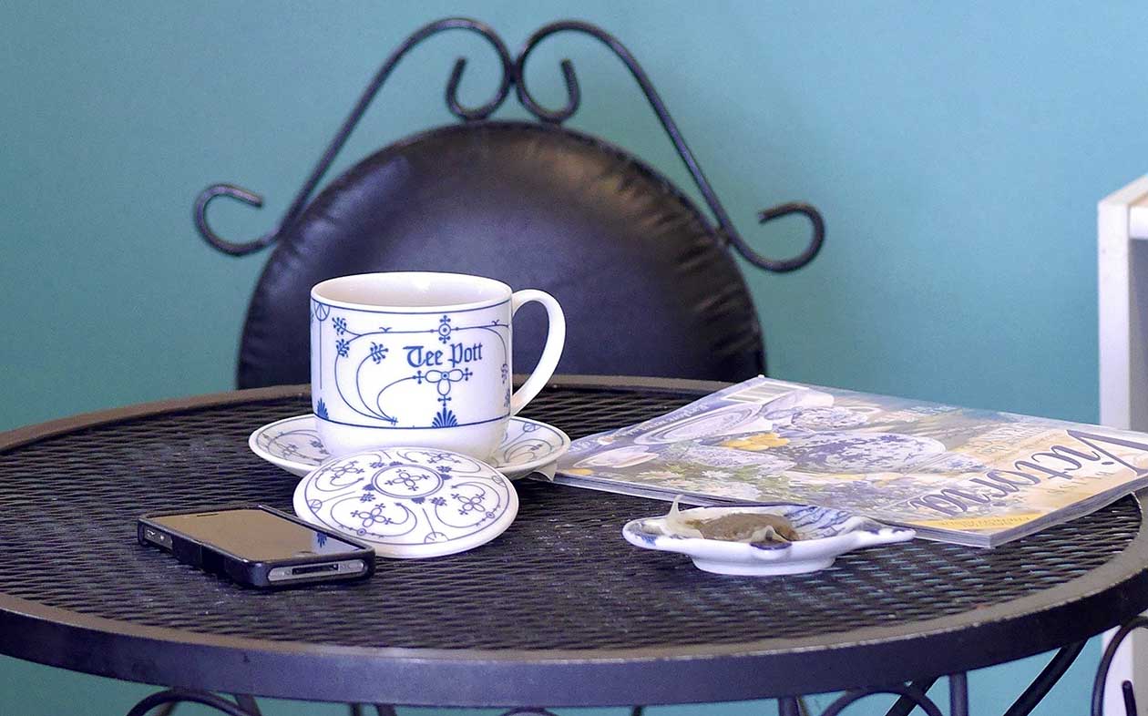 covered tea mug with tea bag in tea bag holder and a magazine on a bistro table top
