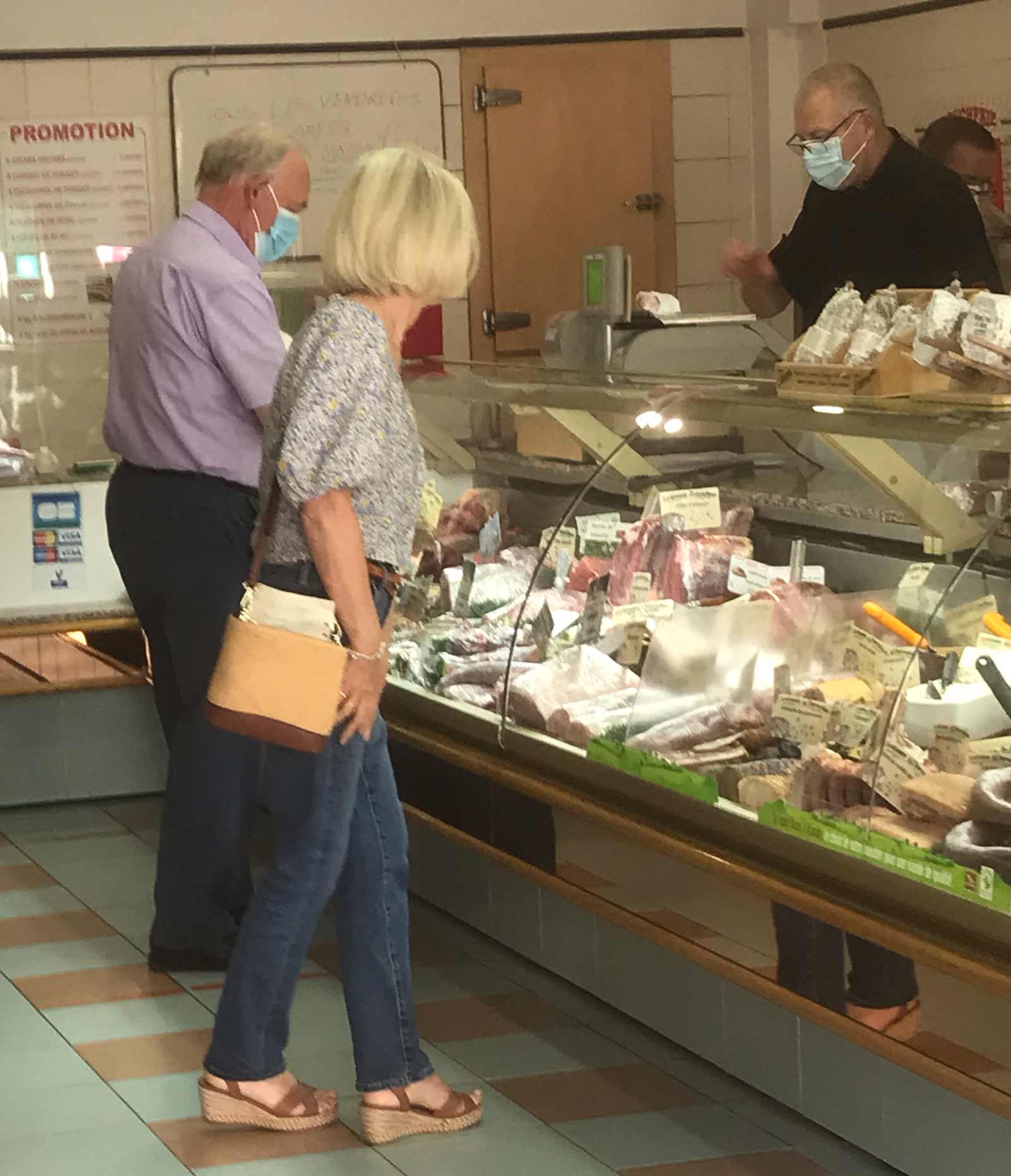 woman at bucher shop wearing jeans, cotton print top, leather sands and straw handbag