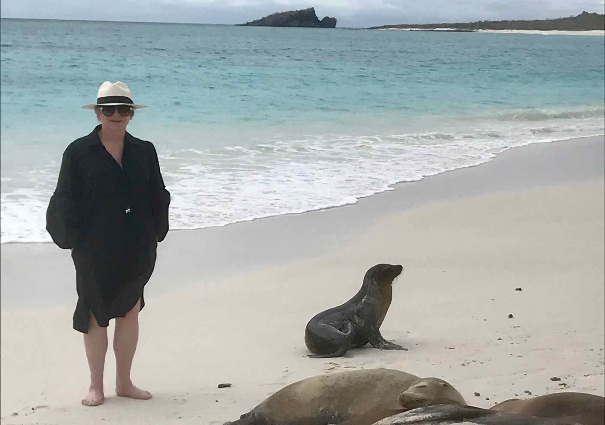 Chic woman in black dress, hat and sunglasses with seals at Galápagos