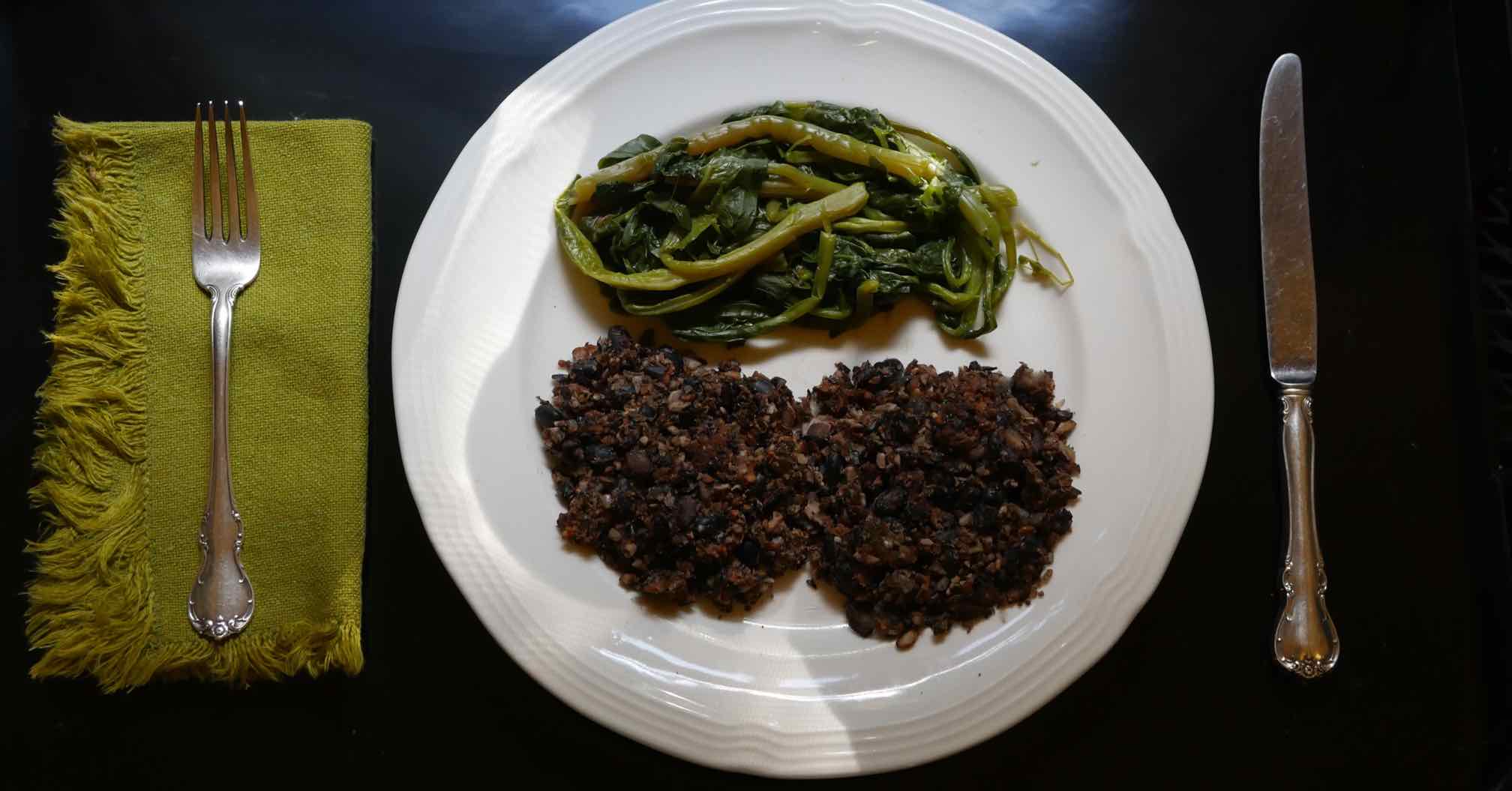 white plate with cooked poke greens and two black bean croquettes