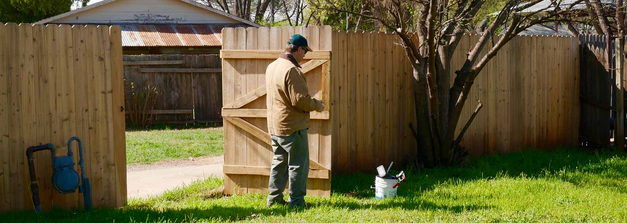 man repairing gate latch on cedar fence