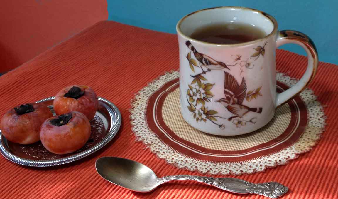 tea in mug with dish of persimmons at side