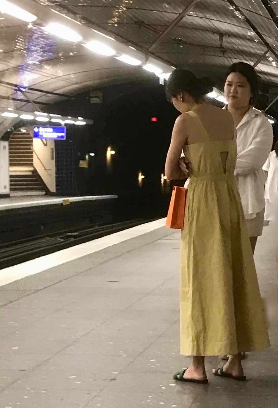 2 women in Paris Metro, one wearing yellow sundress, other wearing white jacket and skirt